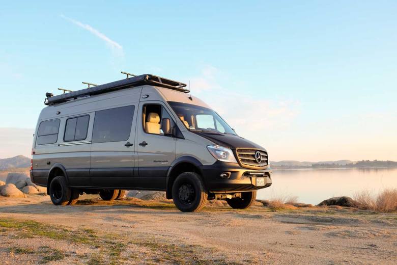 A profile view of a custom Sportsmobile Sprinter 4x4 camper conversion besides a river embankment.