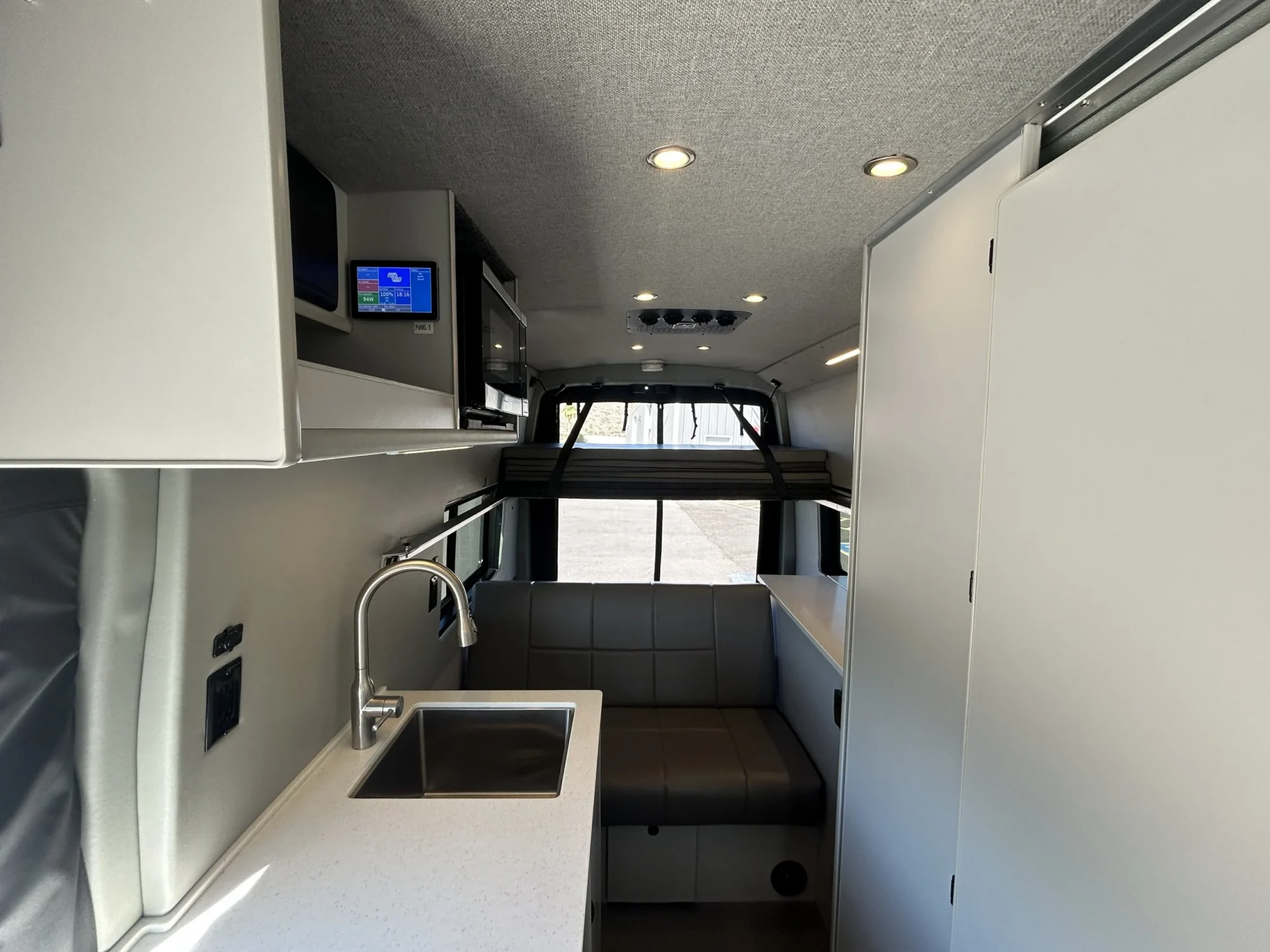 2024 Ford Transit 350 148 High Roof AWD, cabin view toward rear showing galley sink, microwave, sofa, and upper bed