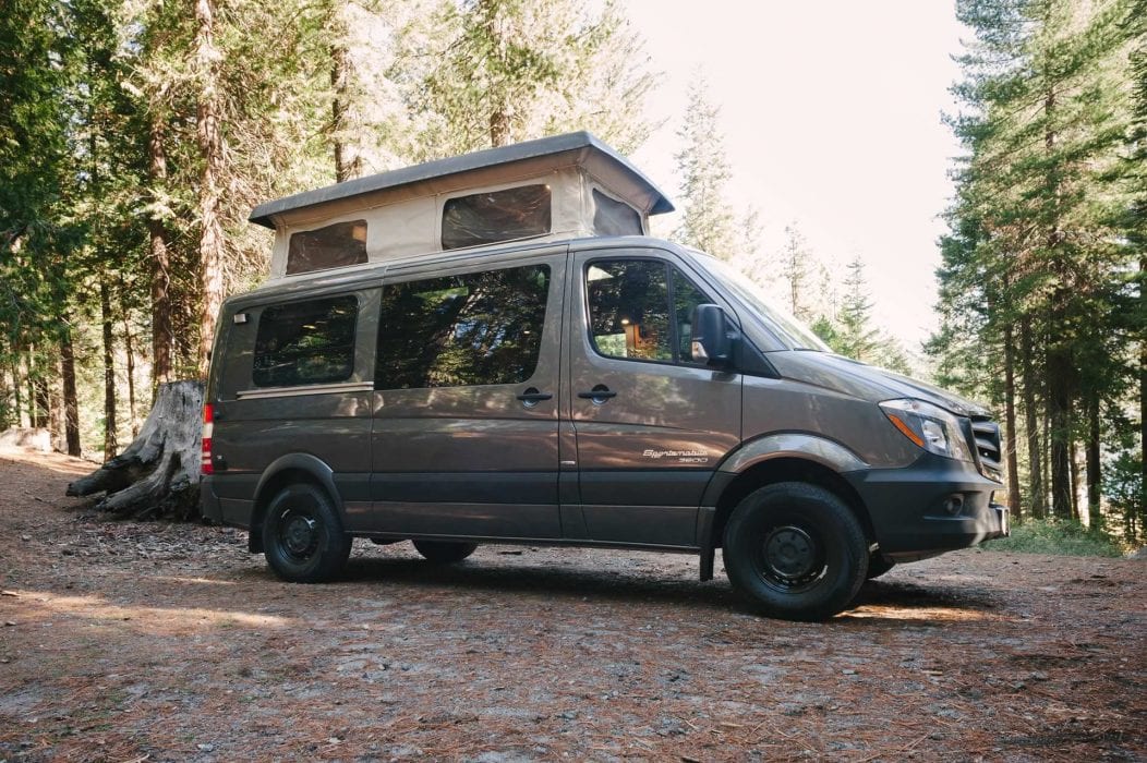 Grey Sportsmobile camper van with a penthouse top in the woods.