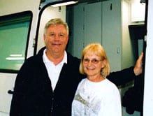 Julia and Tom Hendricks smile happily next to their white Sportsmobile custom camper conversion.