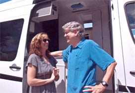 The Harrisons stand in the doorway of their white custom Sportsmobile camper van conversion.