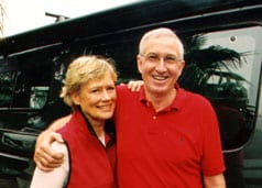 Paul and Marianne Reasoner stand under their awning next to their dark grey Sportsmobile conversion van.