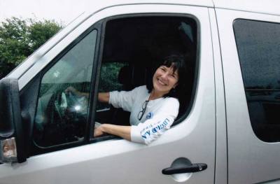 Lady Sportsmobile owner, Donna Nelson, stands next to her custom silver Sportsmobile conversion van.