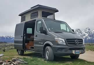 Dark grey Sprinter custom camper with penthouse top expanded and door open.