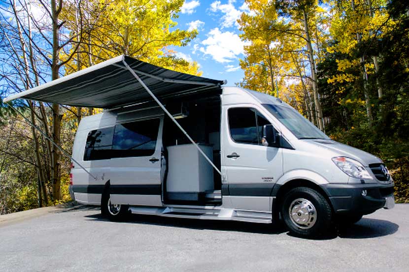 A custom silver Sportsmobile conversion van with a Fiamma awning extended.