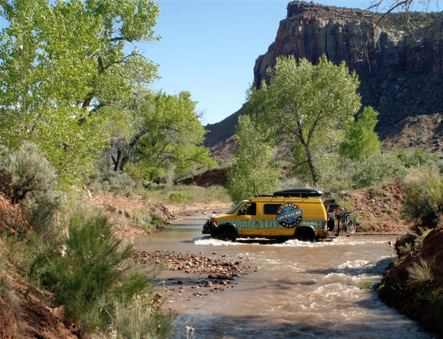 Yellow Sportsmobile 4x4 goes over water.