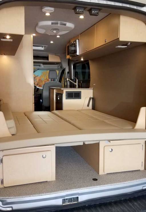 Inside a custom silver Sportsmobile Transit conversion van with a couch that converts quickly into a bed.