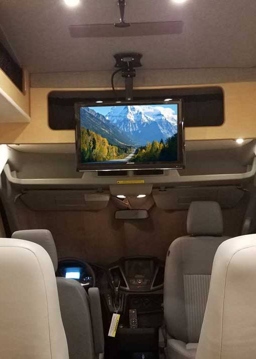 Interior view of a custom Sportsmobile Transit conversion van with Captain seats and a flat screen TV.