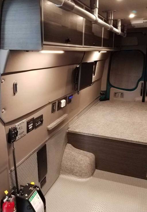 Interior view of a Sportsmobile Sprinter with cabinets and storage.