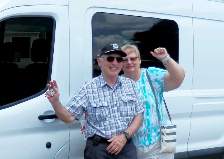 Happy Sportsmobile Transit owners Hal and Jeane standing next to their van conversion.