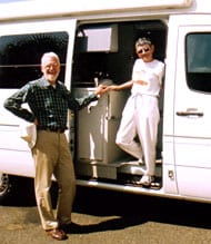The Bayers standing next to their white Sportsmobile conversion camper van.