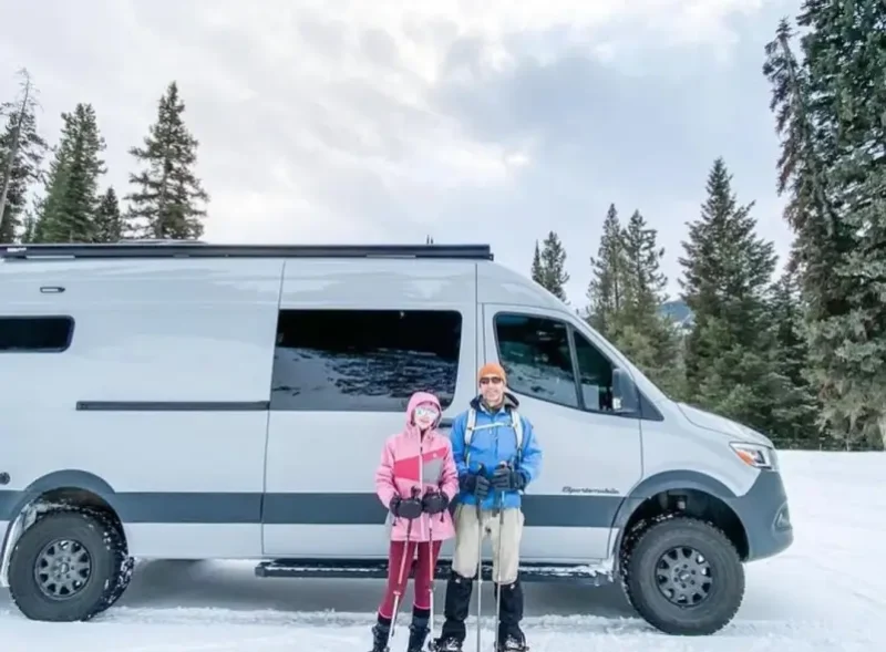 A couple of skiers standing in front of a white van.