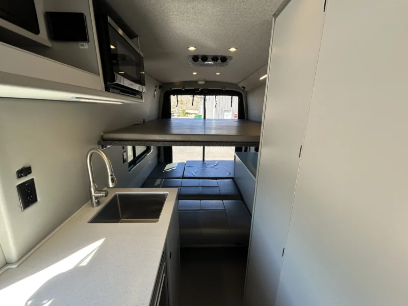 2024 Ford Transit 350 148 High Roof AWD, mid-cabin view showing galley, tall bath door, and two-tier rear beds deployed