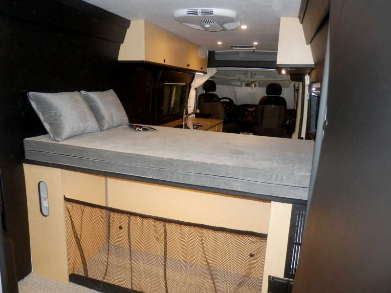 Rear view of a custom Sportsmobile Promaster conversion van featuring a platform bed with large compartments for storage.