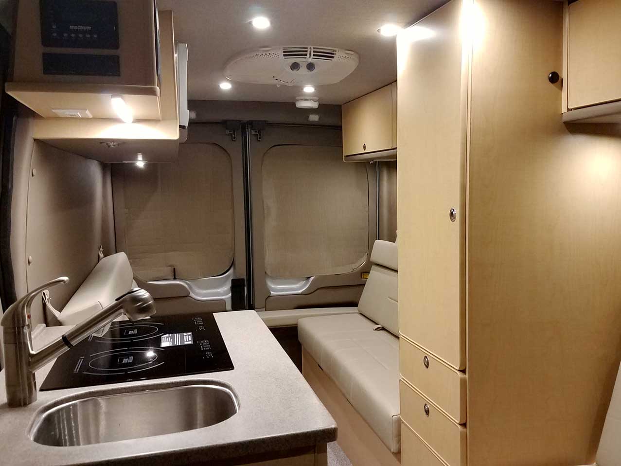 Inside a custom silver Sportsmobile Transit conversion van with dinette that seats six people.