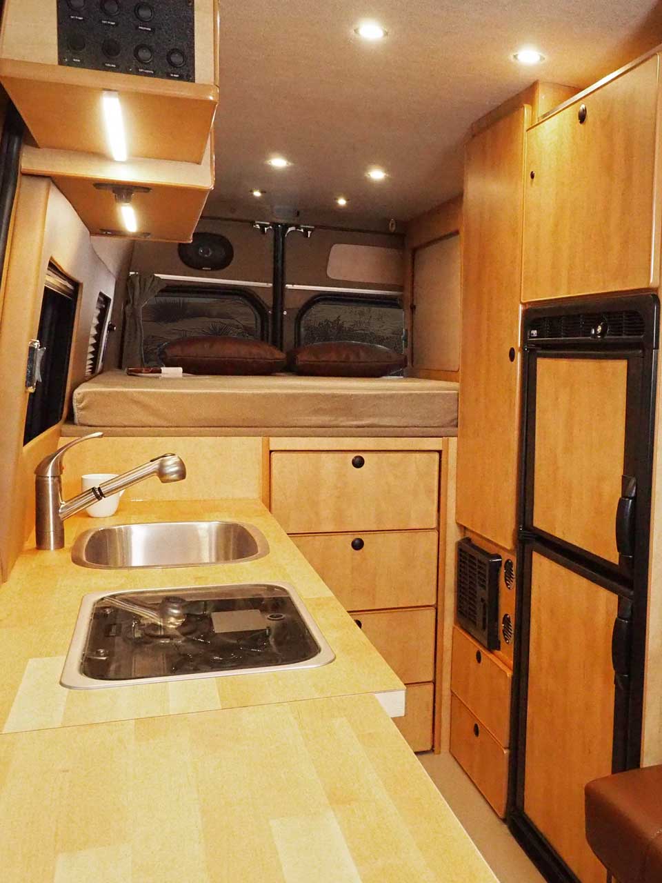 Sprinter interior with maple cabinets and a refrigerator.