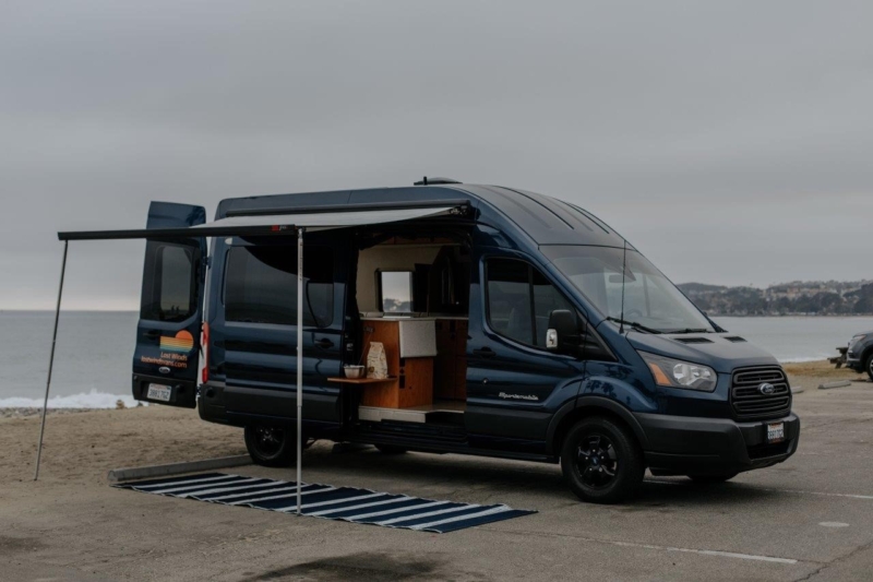 Dark blue 2017 Ford Transit with opened doors parked next to a lake.