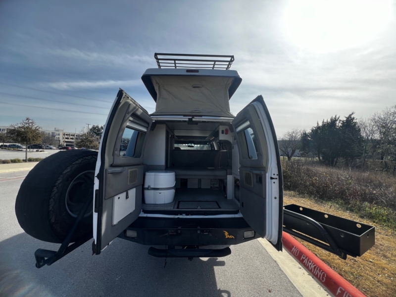 Opened back door of a black 2003 Ford E350 van parked on the side of the road.