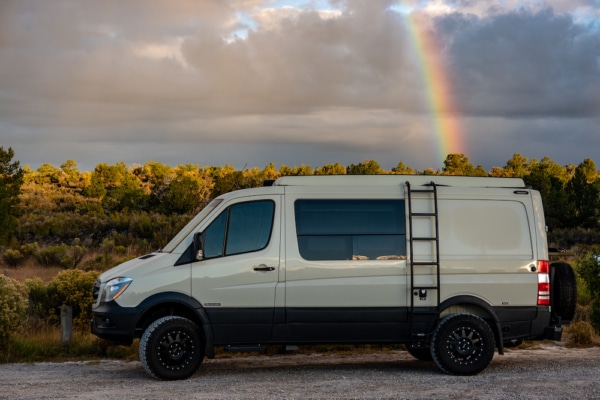 Converted Mercedes Sprinter parked on the side of the road. Rainbow in the background.