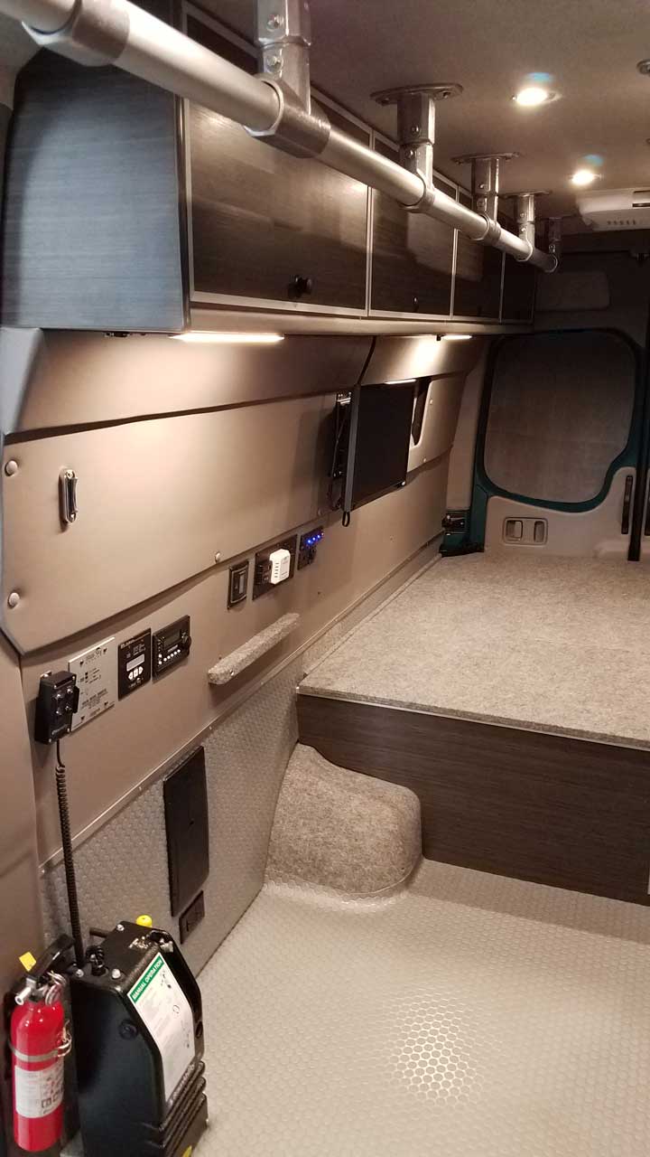 Interior view of a Sportsmobile Sprinter with cabinets and storage.